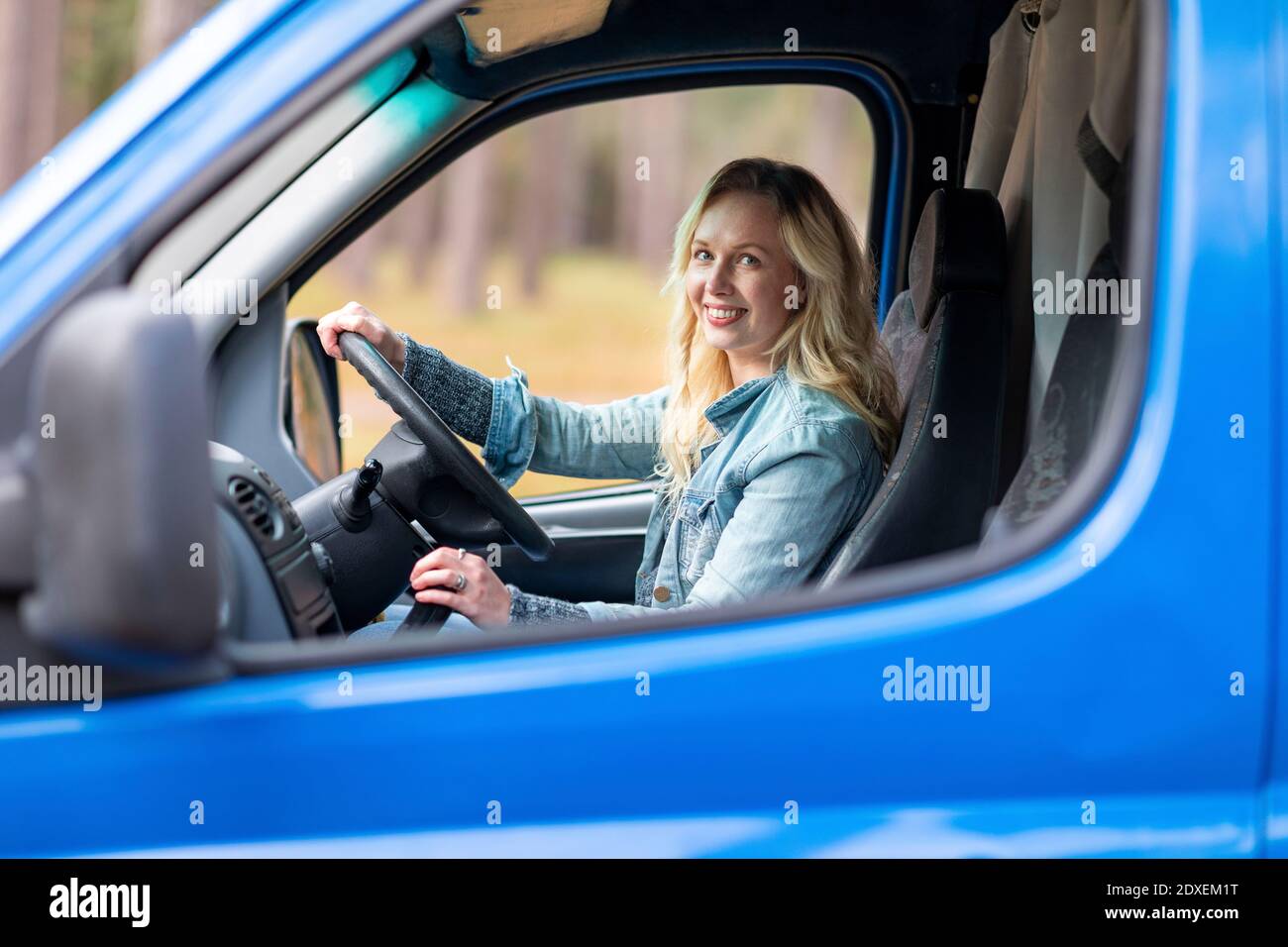Smiling woman holding steering wheel while sitting in camper van Stock Photo