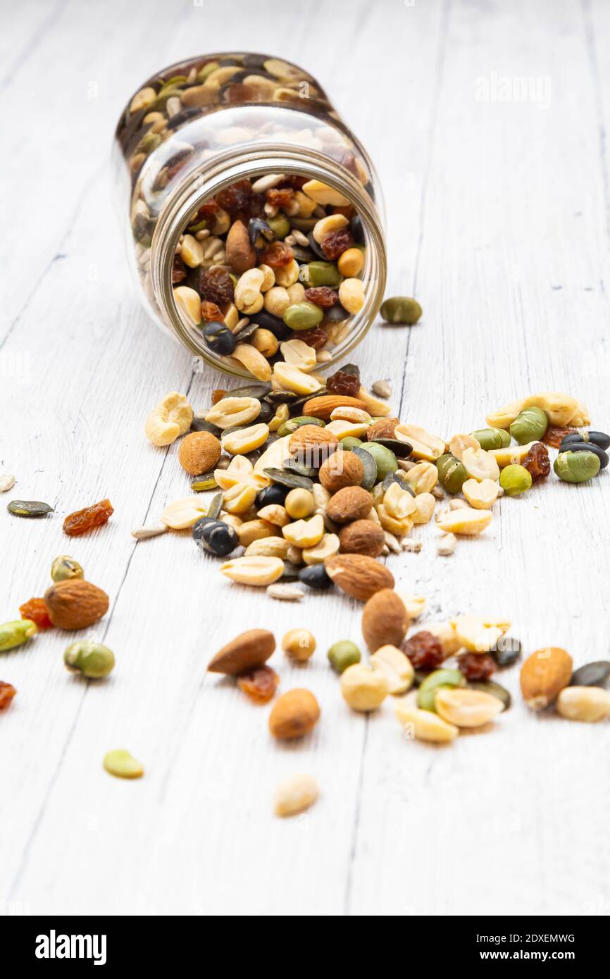Jar of raisins, peanuts, cashew nuts, almonds, soybeans, sunflower seeds and pumpkin seeds spilled on wooden background Stock Photo