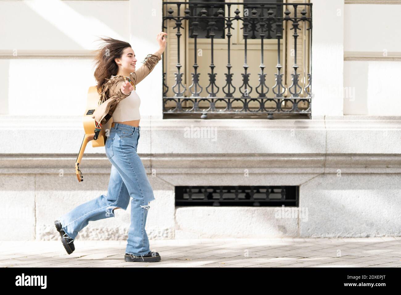 Cheerful female musician with arms outstretched running on footpath by building in city Stock Photo