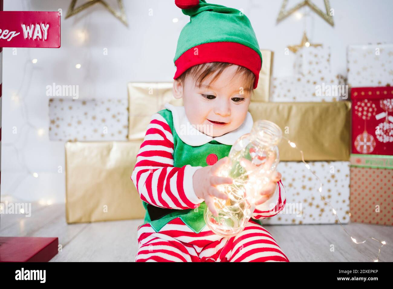 Baby boy in elf costume playing with illuminated string lights in bottle  while sitting at home during Christmas Stock Photo - Alamy