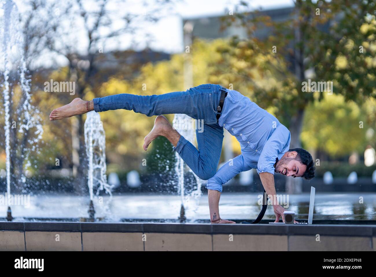 Young businessman using laptop while doing handstand on retaining wall Stock Photo