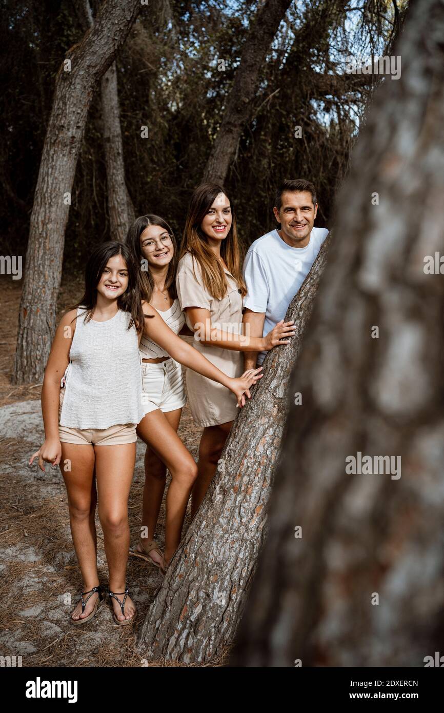 Parents with children standing behind tree trunk in forest Stock Photo