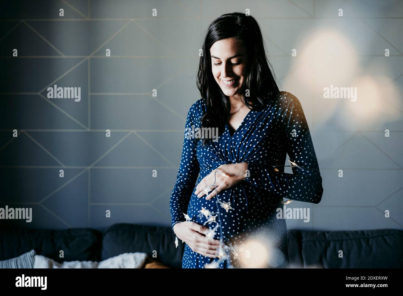 Smiling pregnant woman with lighting equipment standing against wall at home Stock Photo