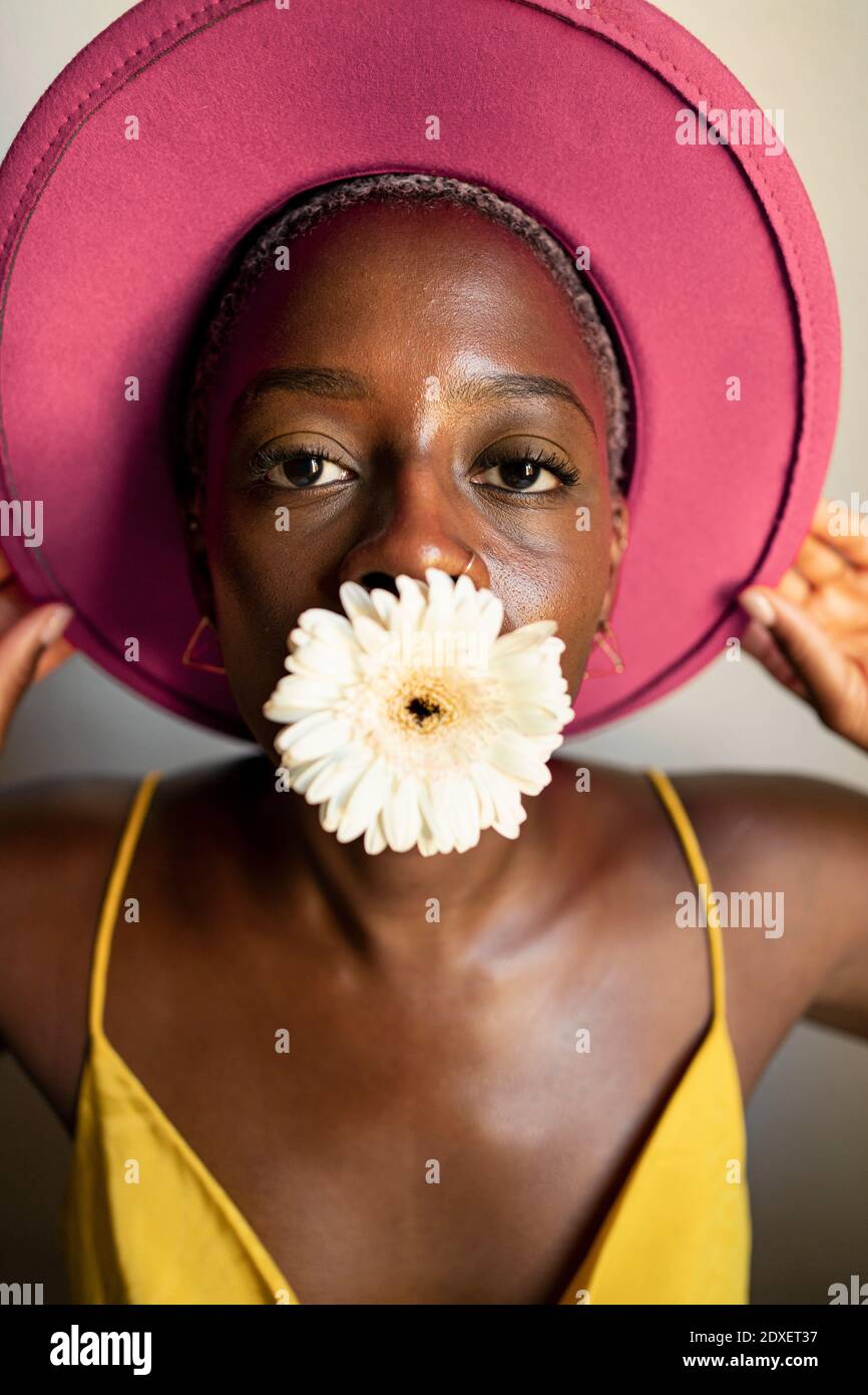 Woman with white flower in mouth wearing pink hat at home Stock Photo -  Alamy