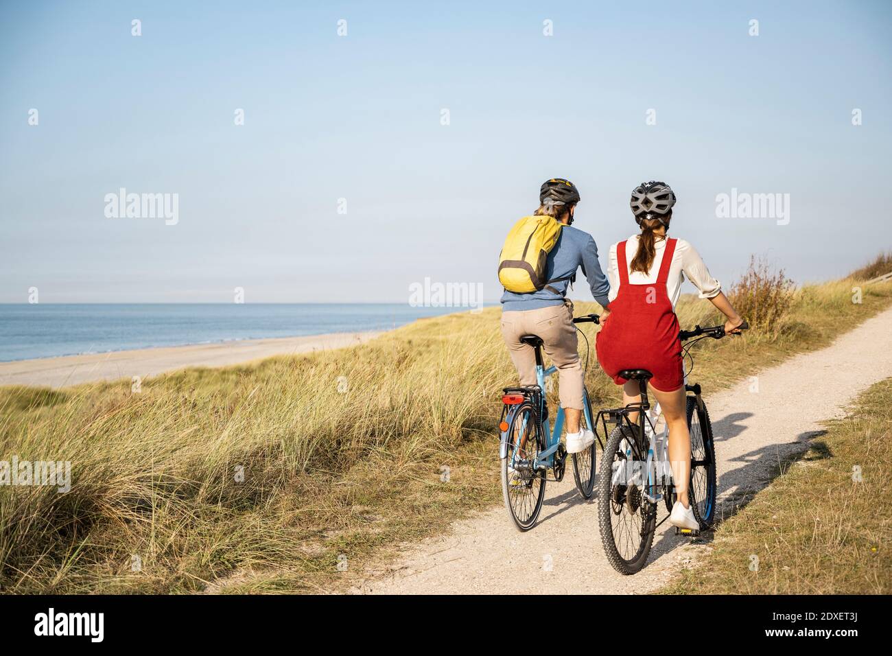 Young couple wearing cycling helmet riding bicycles against clear sky Stock Photo