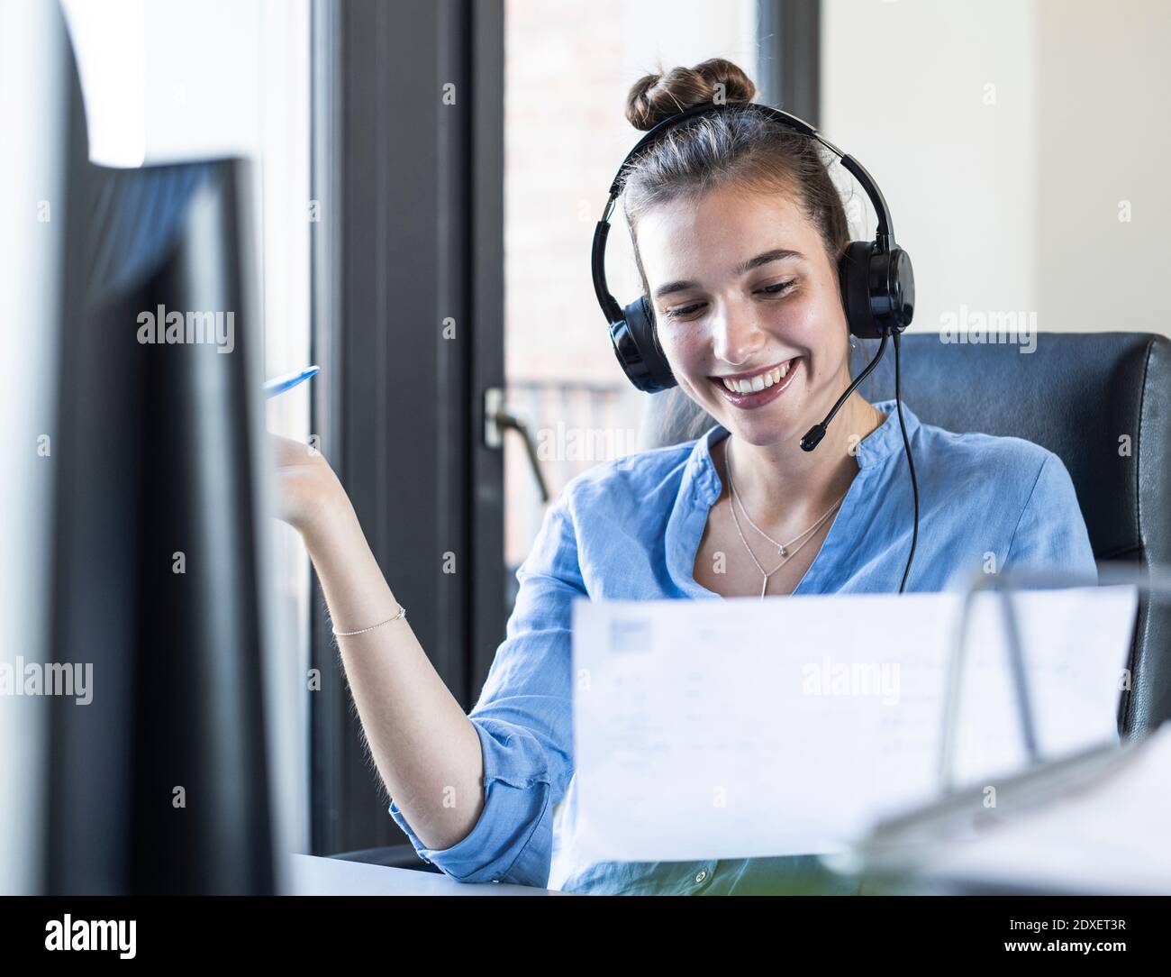 Businesswoman with paper talking through headphones while sitting at office Stock Photo
