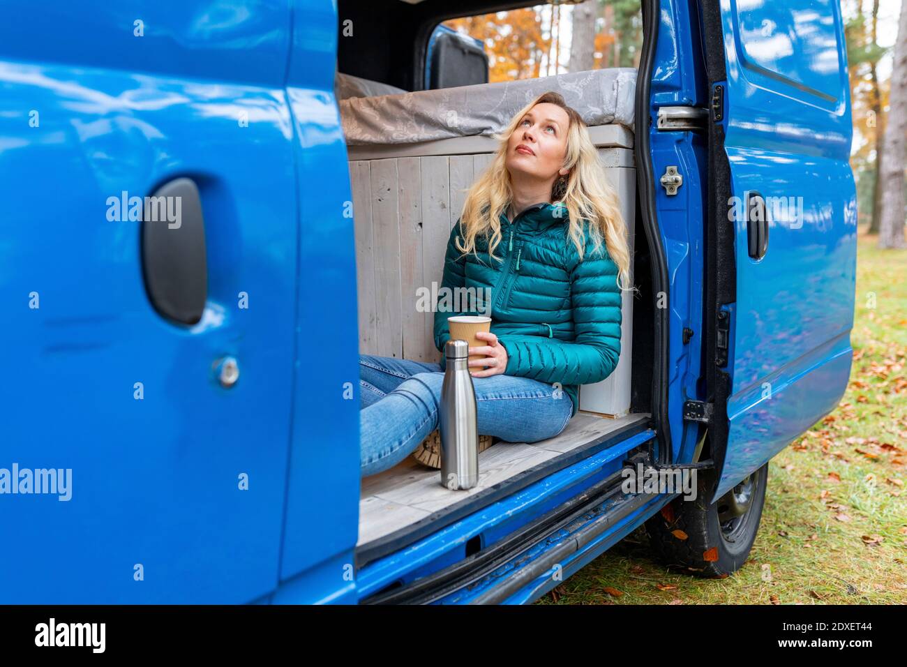 Woman with tea cup day dreaming while sitting at door of motor home Stock Photo