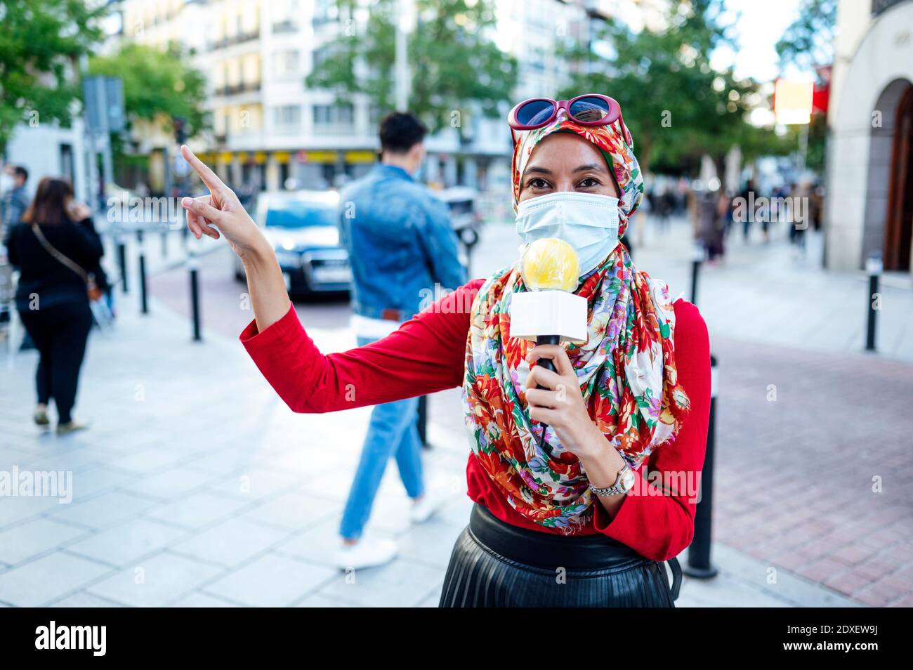 Muslim female journalist broadcasting in city during COVID-19 Stock Photo