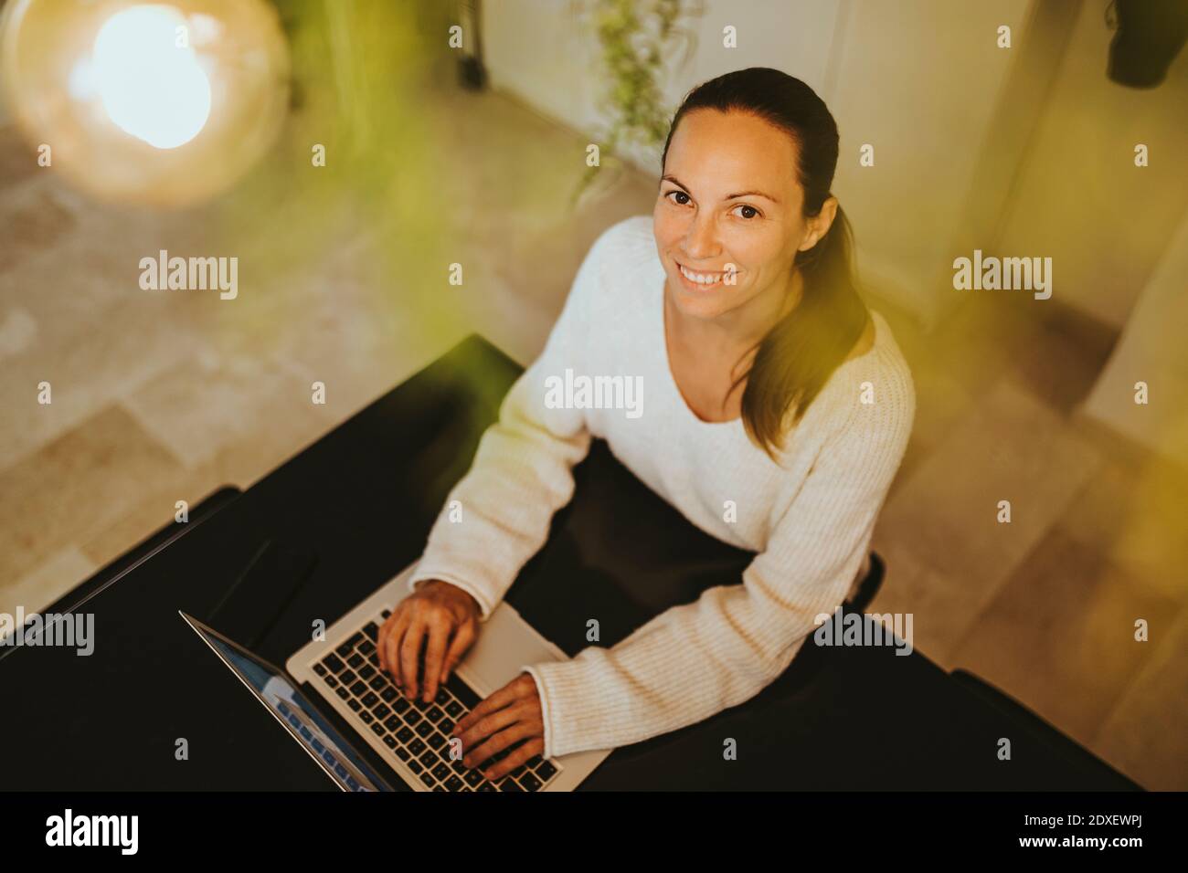 Smiling woman sitting with laptop at kitchen island Stock Photo