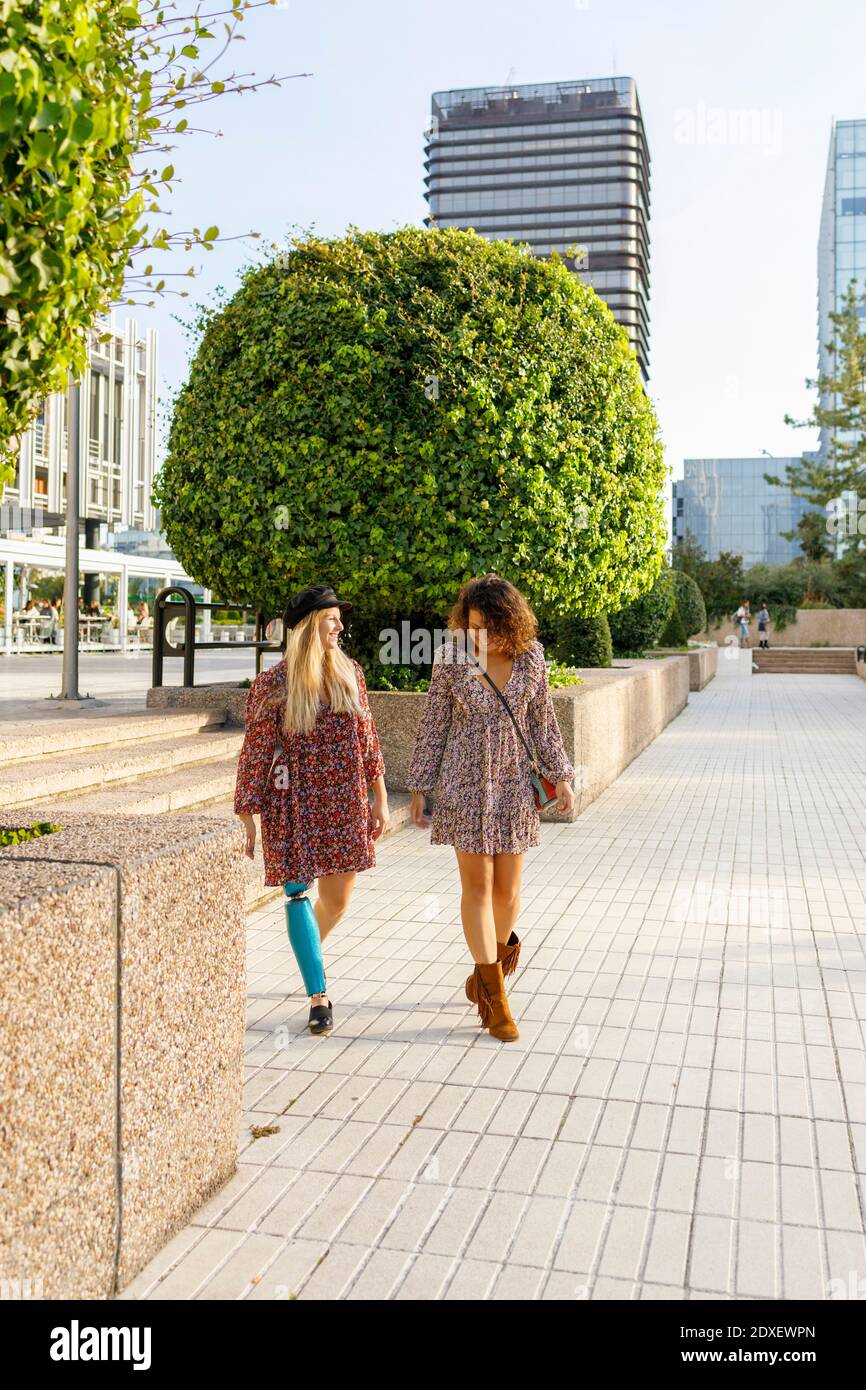 Disabled woman walking with female friend on footpath in city Stock Photo