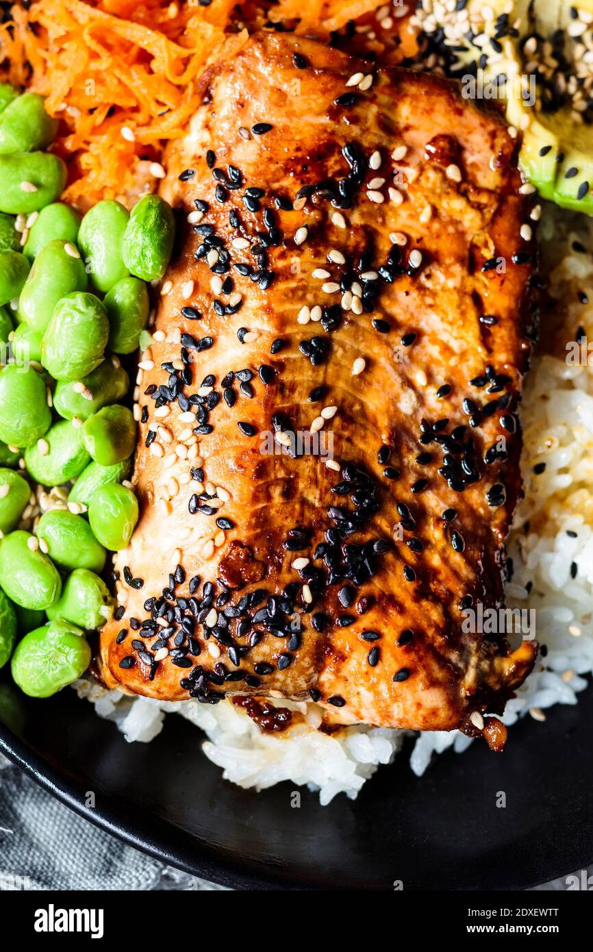 Bowl of teriyaki salmon with rice, carrot salad, edamame beans, avocado