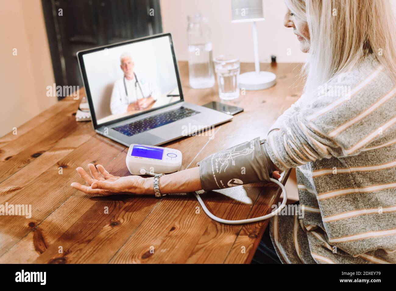 Senior woman checking own blood pressure under guidance of doctor on video call at home Stock Photo