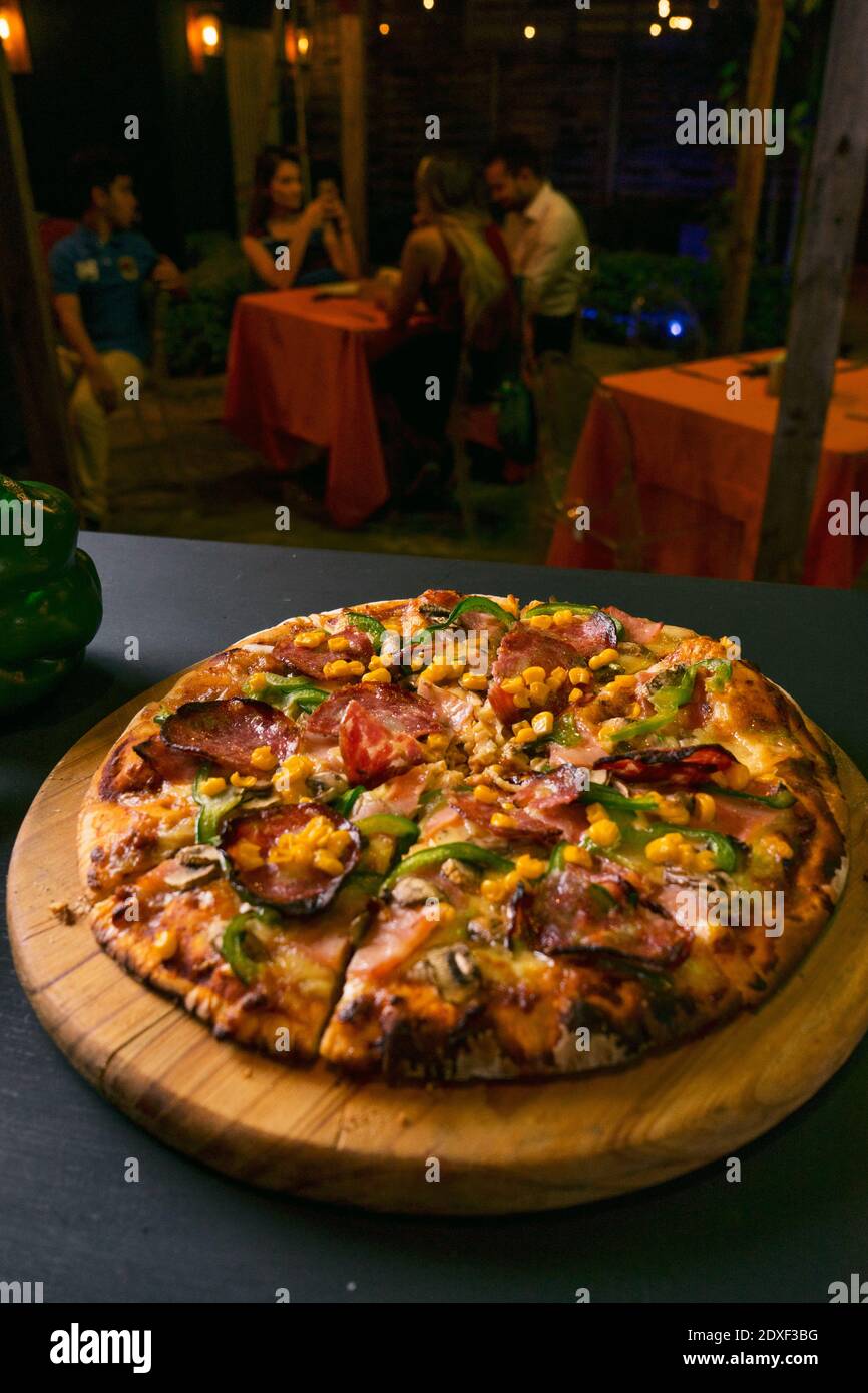 Delicious Italian pizza slice with salami near vegetables on black background restaurant blur Stock Photo