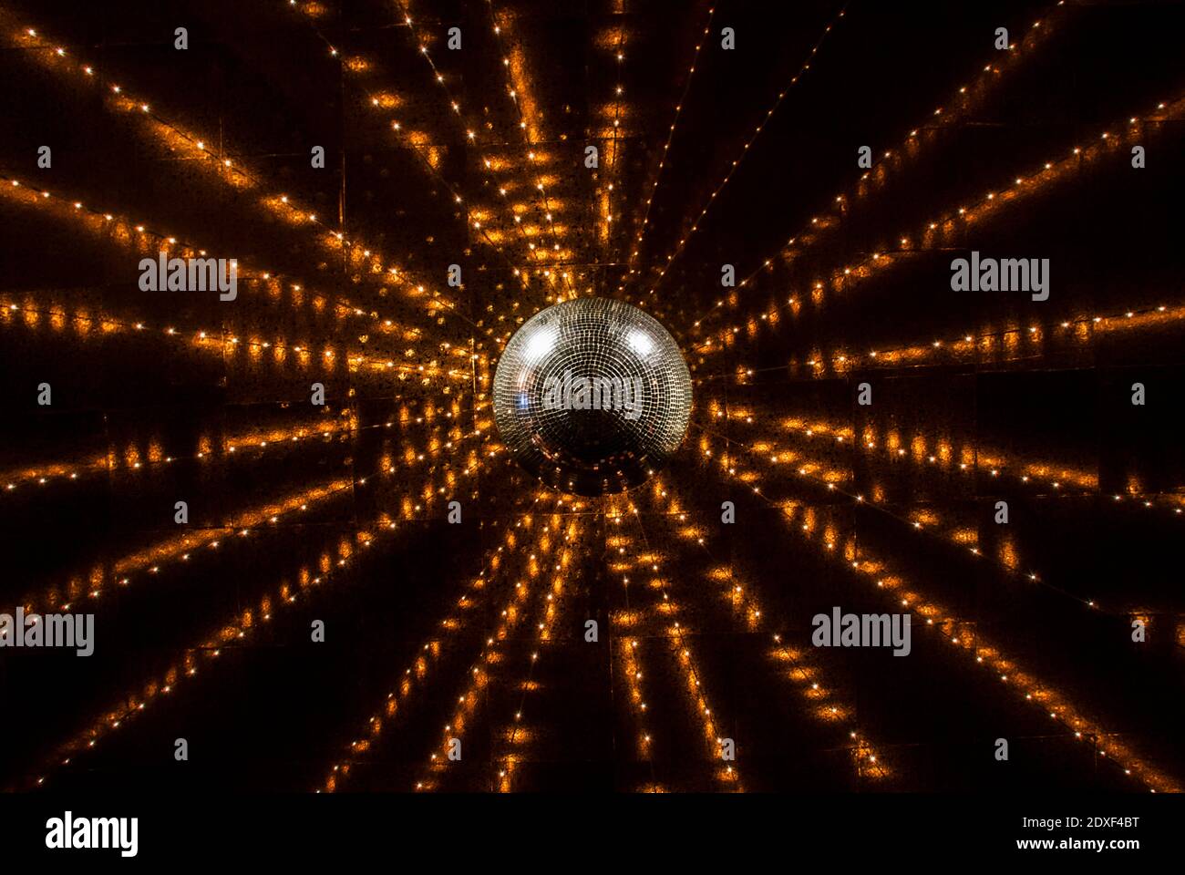 Orange string lights glowing over shiny disco ball Stock Photo