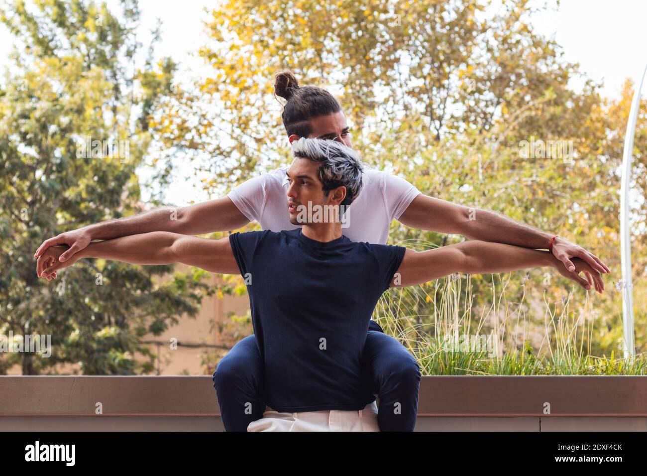 Homosexual couple with arms outstretched by retaining wall against tree Stock Photo