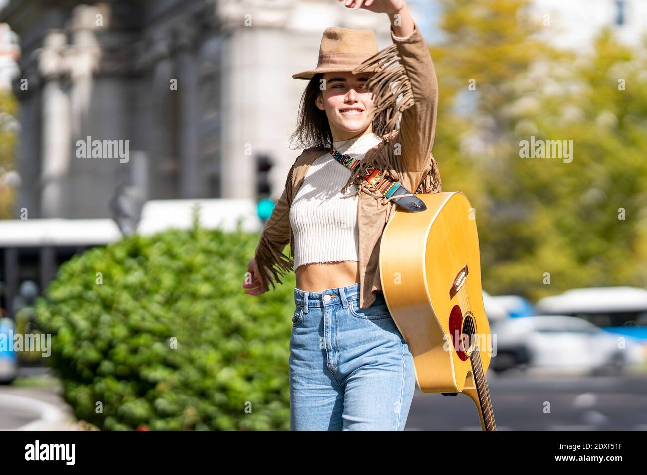 Young woman with hand raised on street in city during sunny day Stock Photo