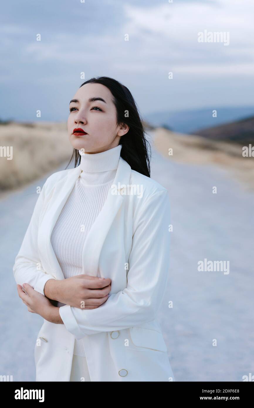 Nostalgic portrait of woman dressed in white in cloudy field at sunset