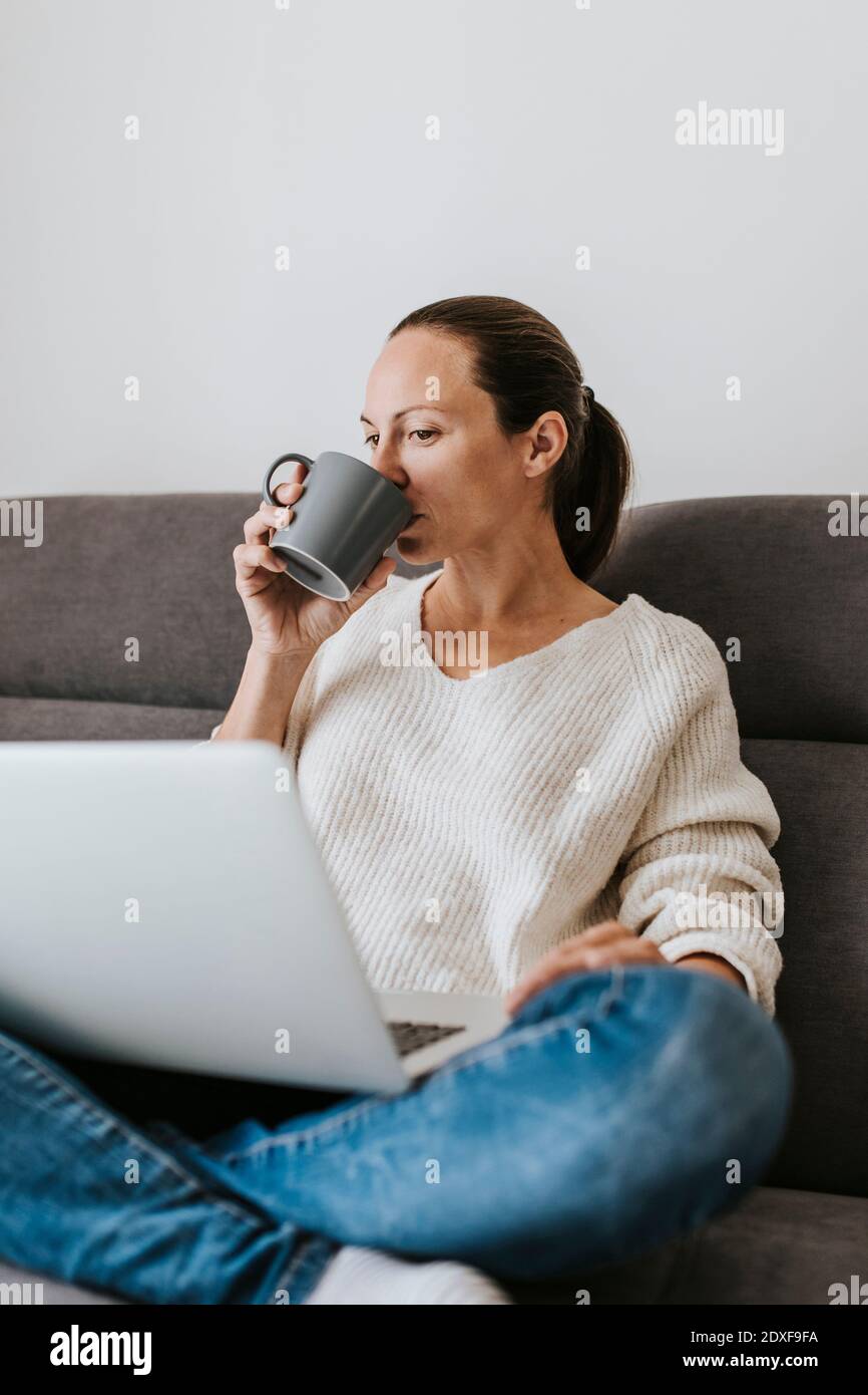 Woman drinking coffee while using laptop at home Stock Photo