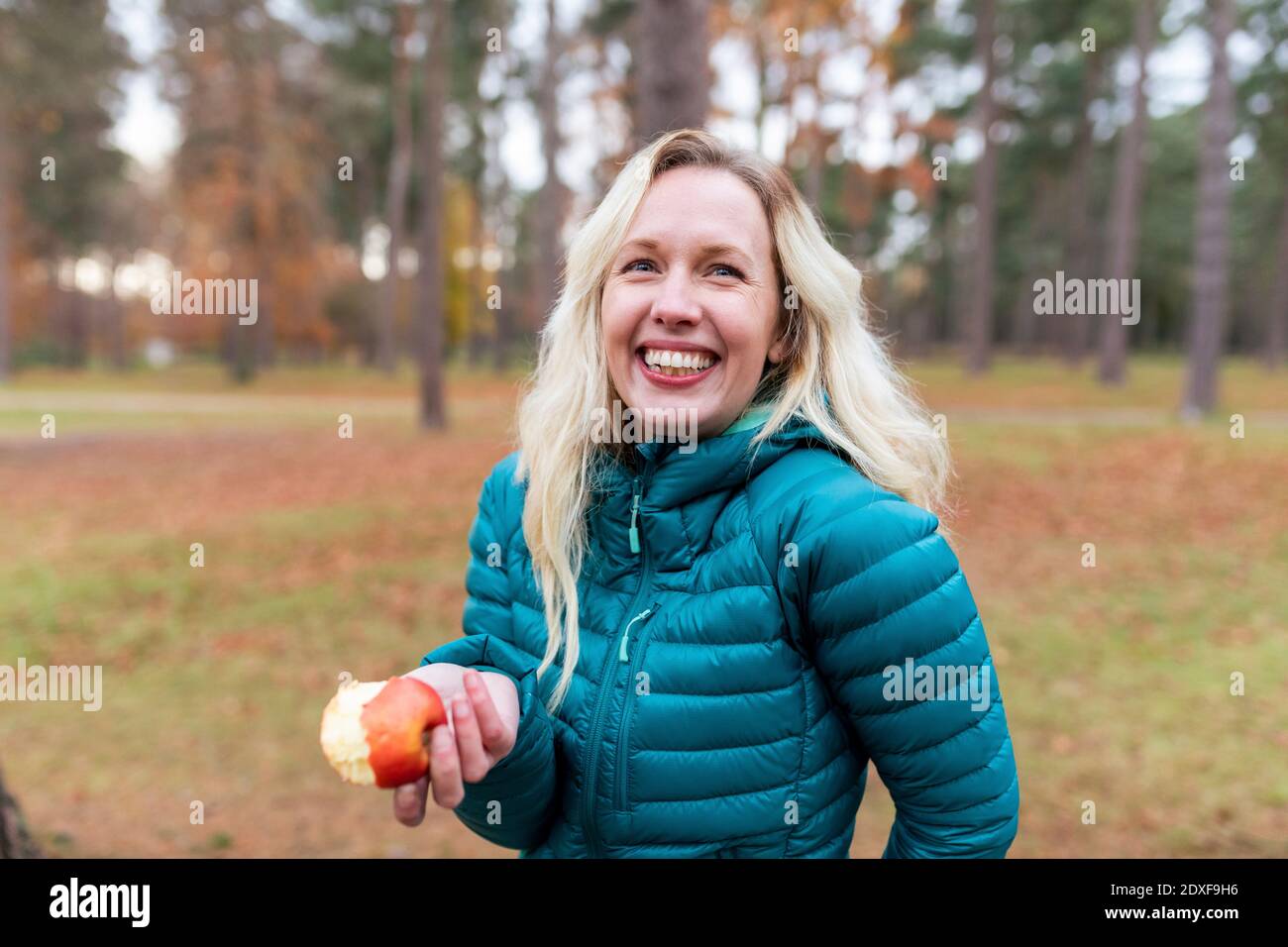 Happy blond haired woman holding apple while standing at Cannock Chase Stock Photo
