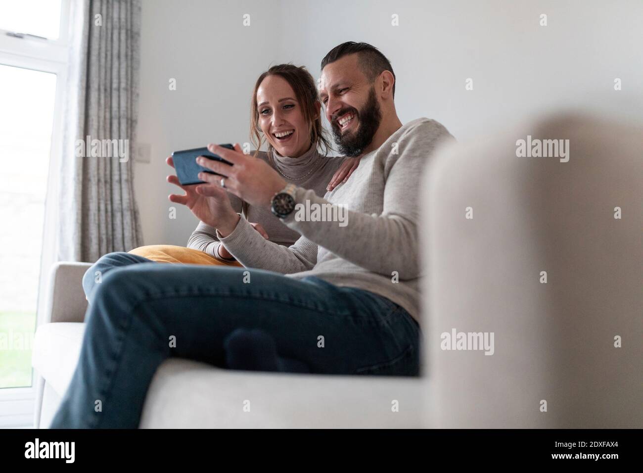 Happy couple using smart phone while sitting at home Stock Photo
