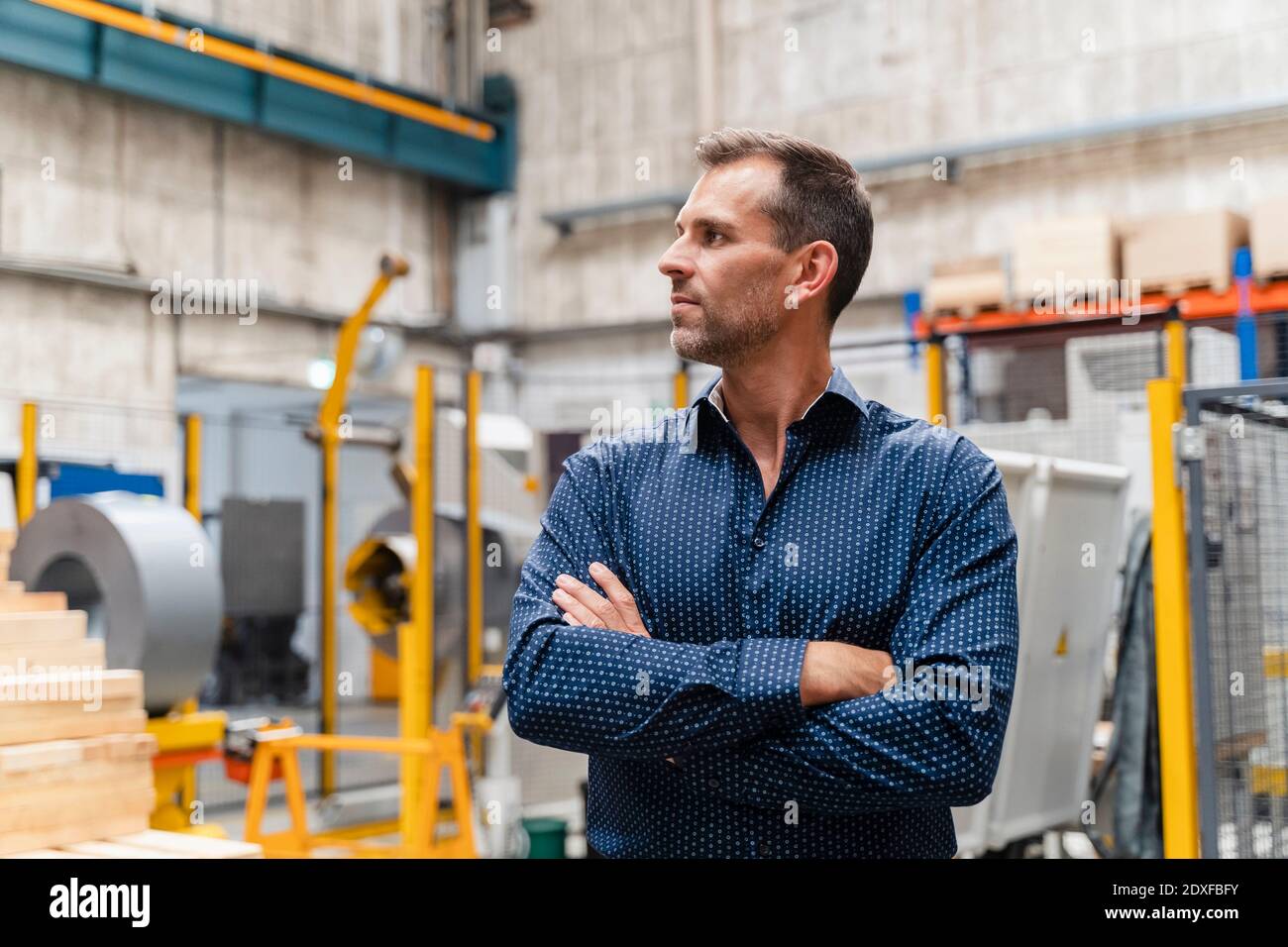 Thoughtful male entrepreneur with arms crossed looking away while ...
