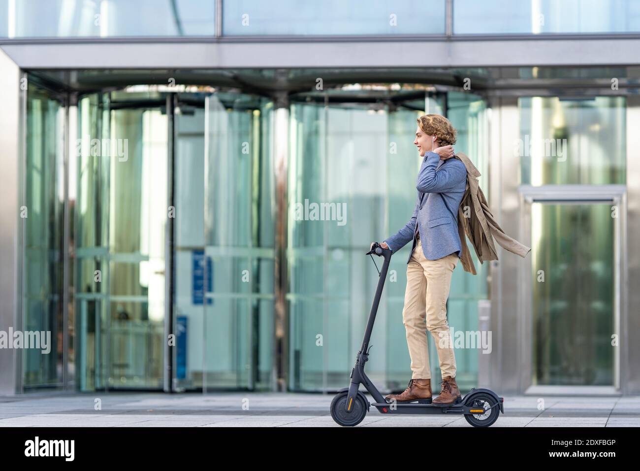 Young businessman riding electric push scooter on footpath Stock Photo