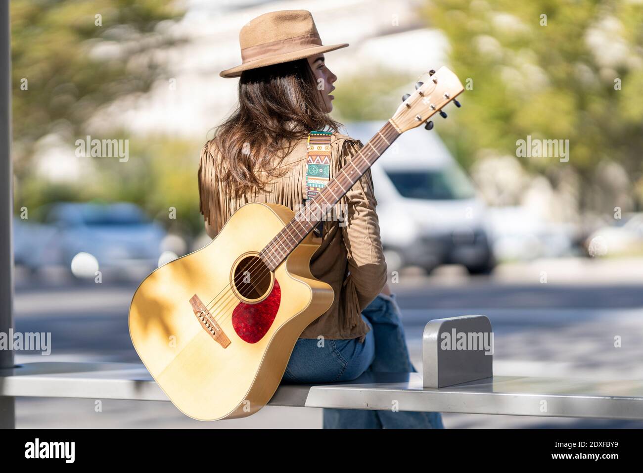 Young woman with guitar sitting at bus stop Stock Photo