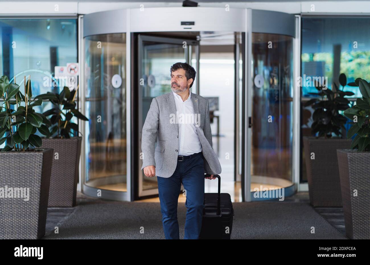 Confident businessman pulling wheeled luggage while entering hotel Stock Photo