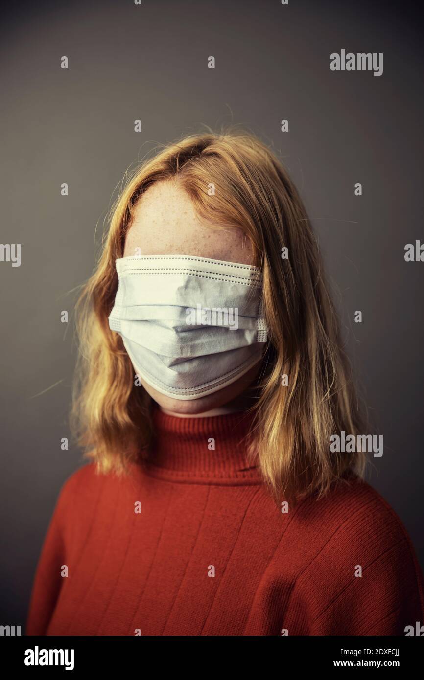 Teenage girl covering entire face with protective face mask while standing against gray background Stock Photo