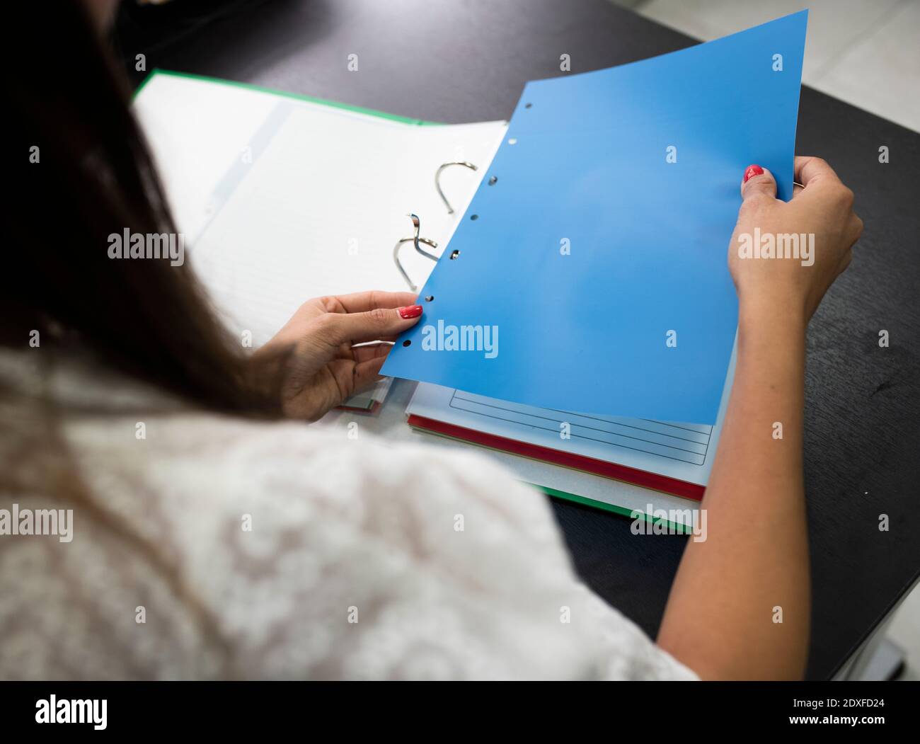 Businesswoman attaching paper in file while sitting on desk at office Stock Photo
