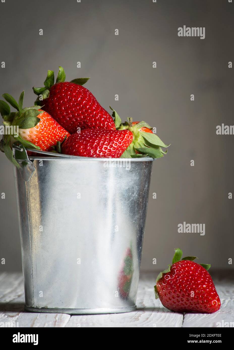 A strawberries inside a small metal bucket that is placed on top of a white wooden board.copy space Stock Photo