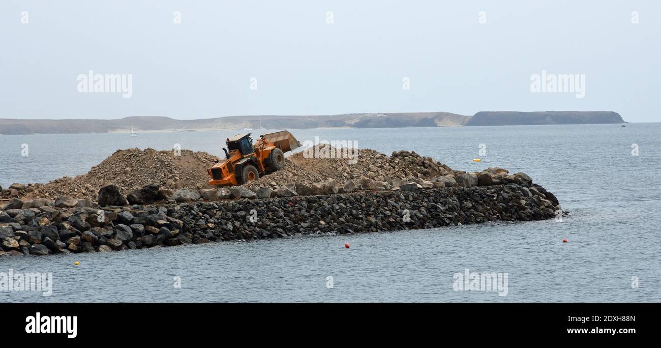 Bulldozer at work moving stone sea in background. building jetty. Stock Photo