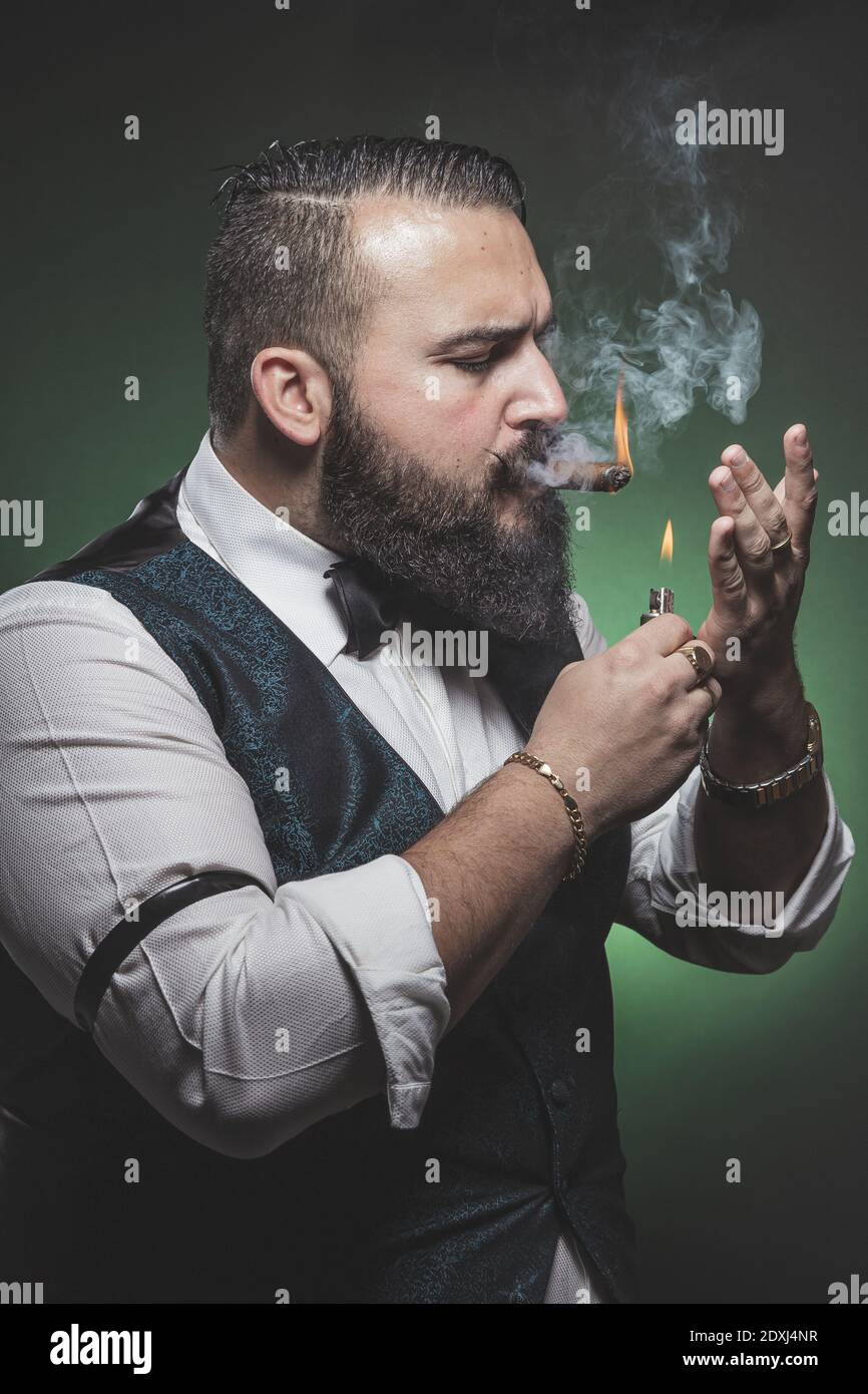 Man with a beard lighting a cigar. Stock Photo