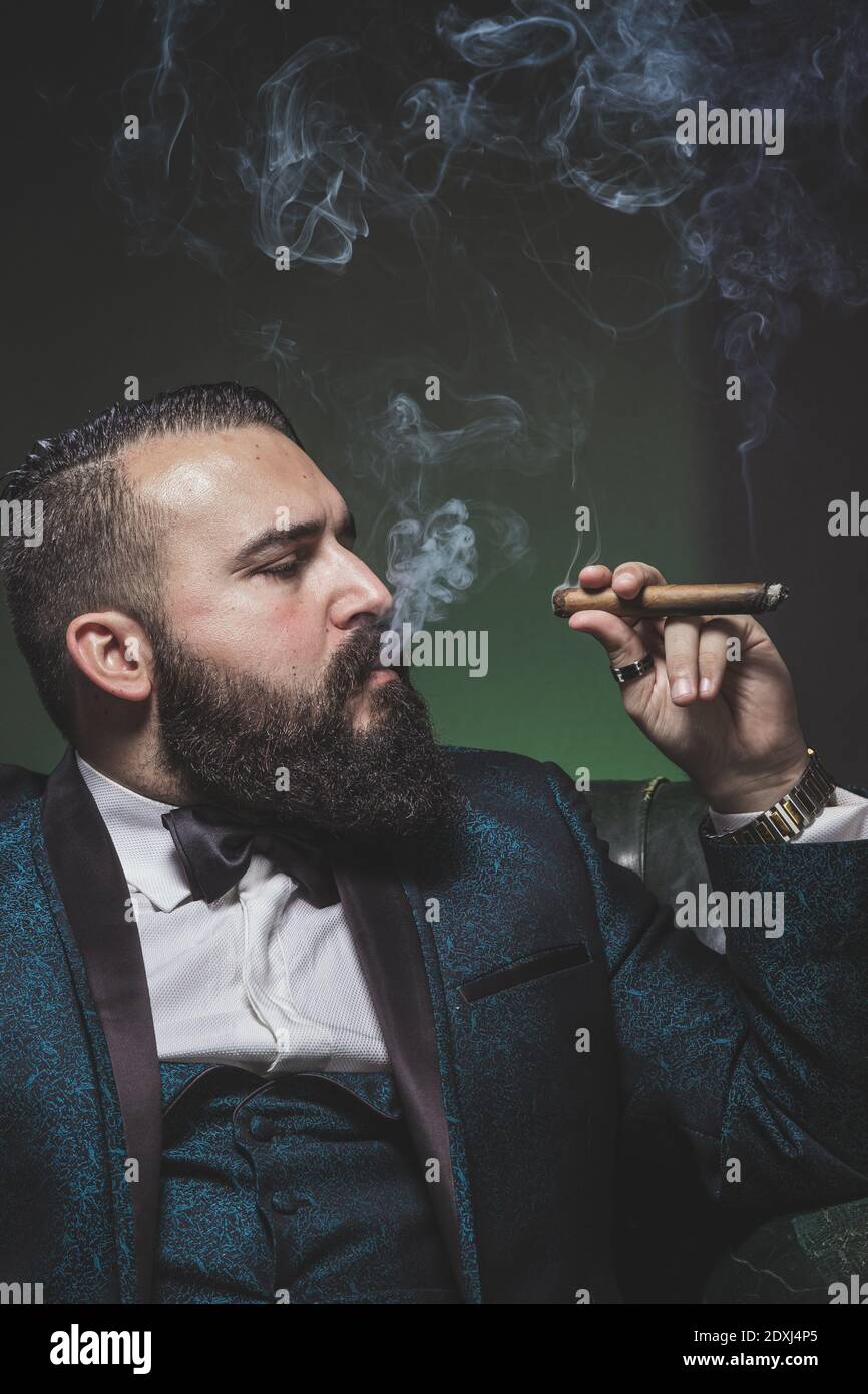 Man with a beard and a green suit, smoking cigars and smoking in profile. Stock Photo