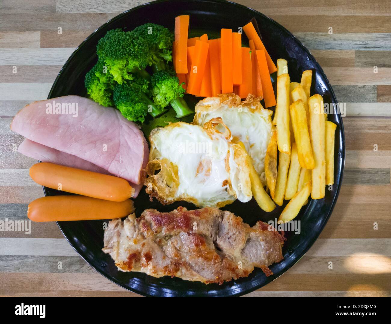 Grilled pork steak with the side dishes (fried egg, french fries, grilled ham, grilled sausage, Boiled carrots and broccoli) for served in the restaur Stock Photo
