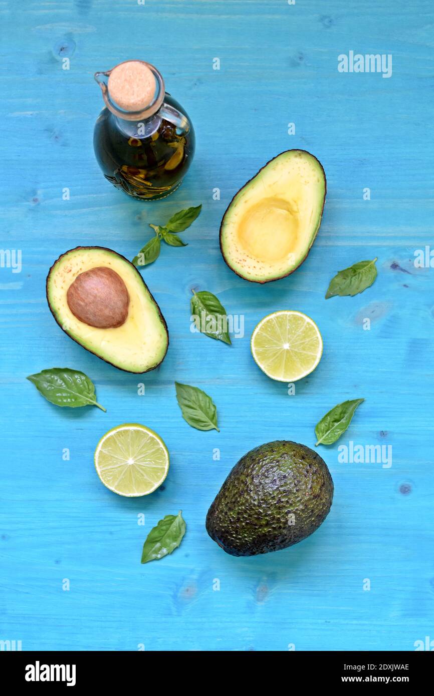 Top table dish with natural avocado, olive oil, limes and mint leaves on blue background. Vertical. Stock Photo