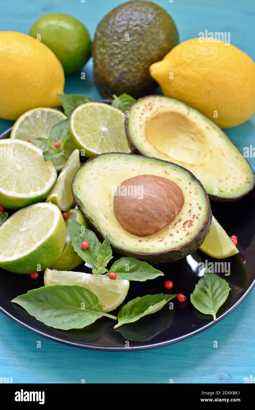 Side view of a black plate full of healthy food. Avocado, sliced limes, lemons and mint on blue background. Stock Photo