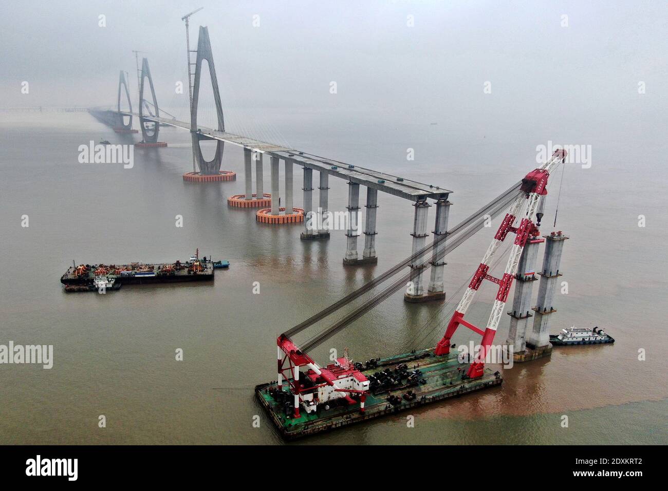 An aerial view of cranes standing on boats erecting piers of the Zhoudai Bridge, Zhoushan city, east China’s Zhejiang province, 23 December 2020. The Stock Photo