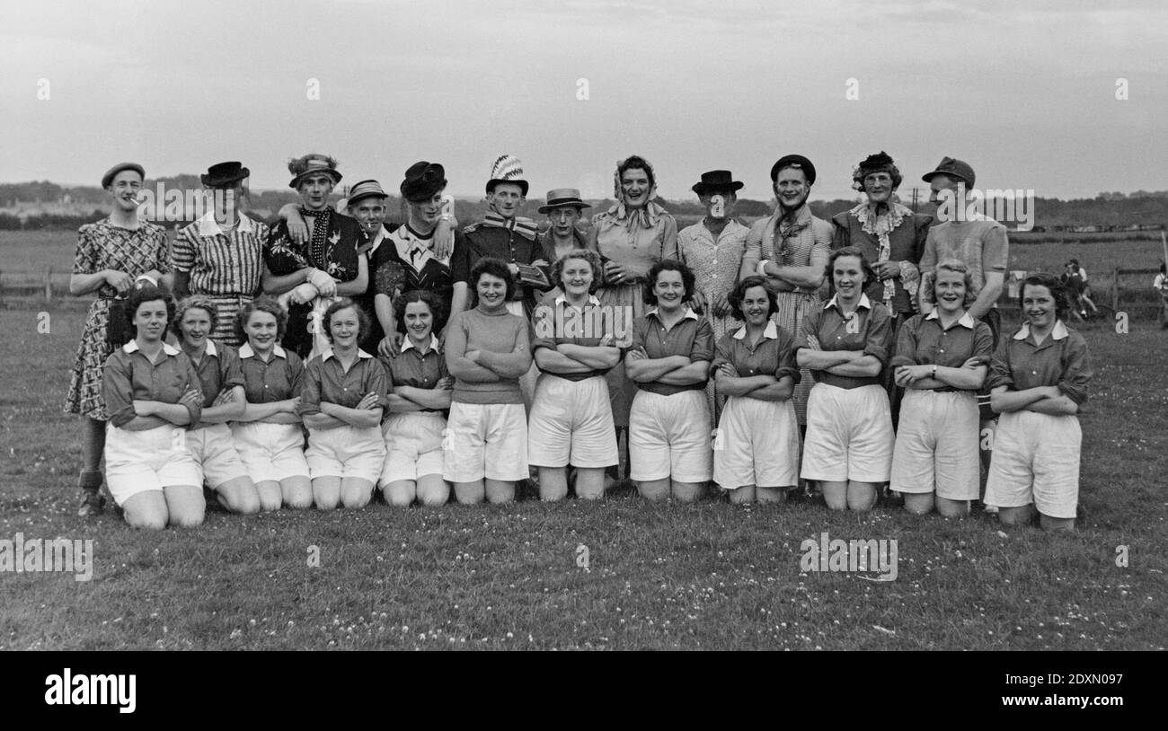 A vintage 1950s English black and white photograph showing a women football, soccer team, posing , kneeling, infront of a mens team who are dressed as women. Stock Photo