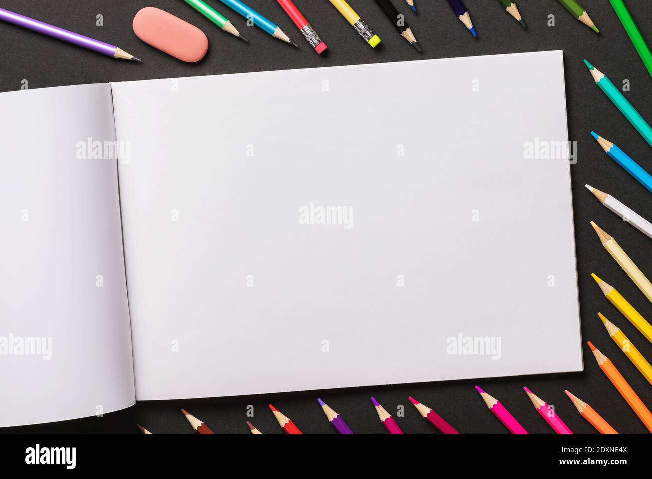 Various colored pencils and sketchbook on a black background with copy space, top view. Stock Photo