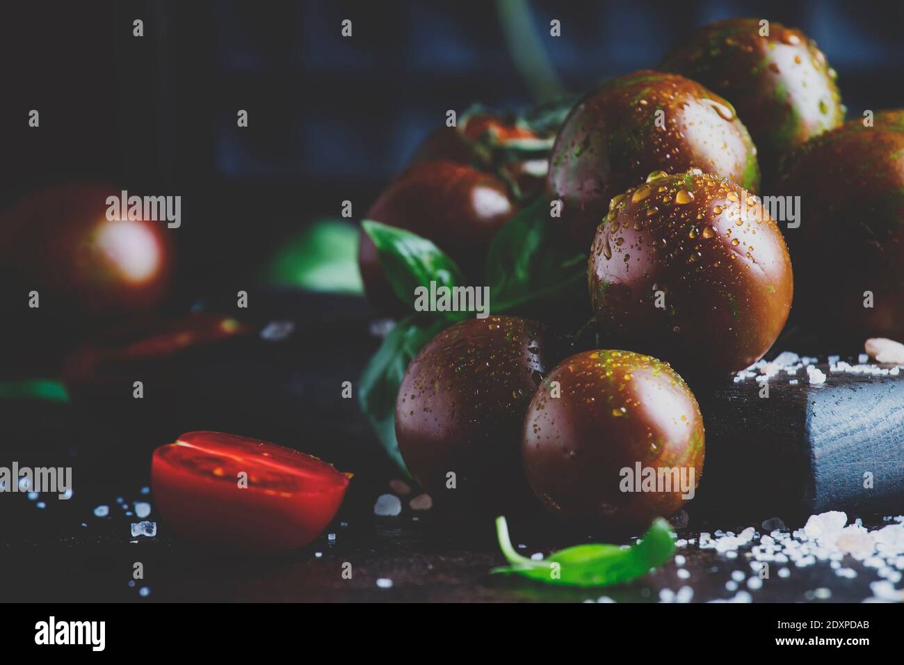 Brown cherry tomatoes with sea salt and green basil on dark table ...