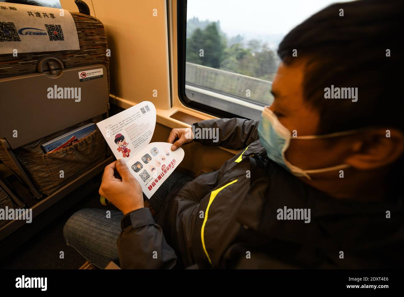 (201224) -- CHENGDU, Dec. 24, 2020 (Xinhua) -- A passenger reads the 'Quiet Car' service prompt card on high-speed train G8609 from Chengdu East Railway Station in southwest China's Sichuan Province to Shapingba Railway Station in southwest China's Chongqing on Dec. 24, 2020. Some high-speed trains in China have piloted 'quiet cars' for passengers who opt for a quiet and undisturbed travel experience. The 'quiet car' is often the No. 3 carriage on the train, with onboard videos muted and announcements made at a lower volume. Doors at the ends of the carriage will be closed to reduce noise fro Stock Photo