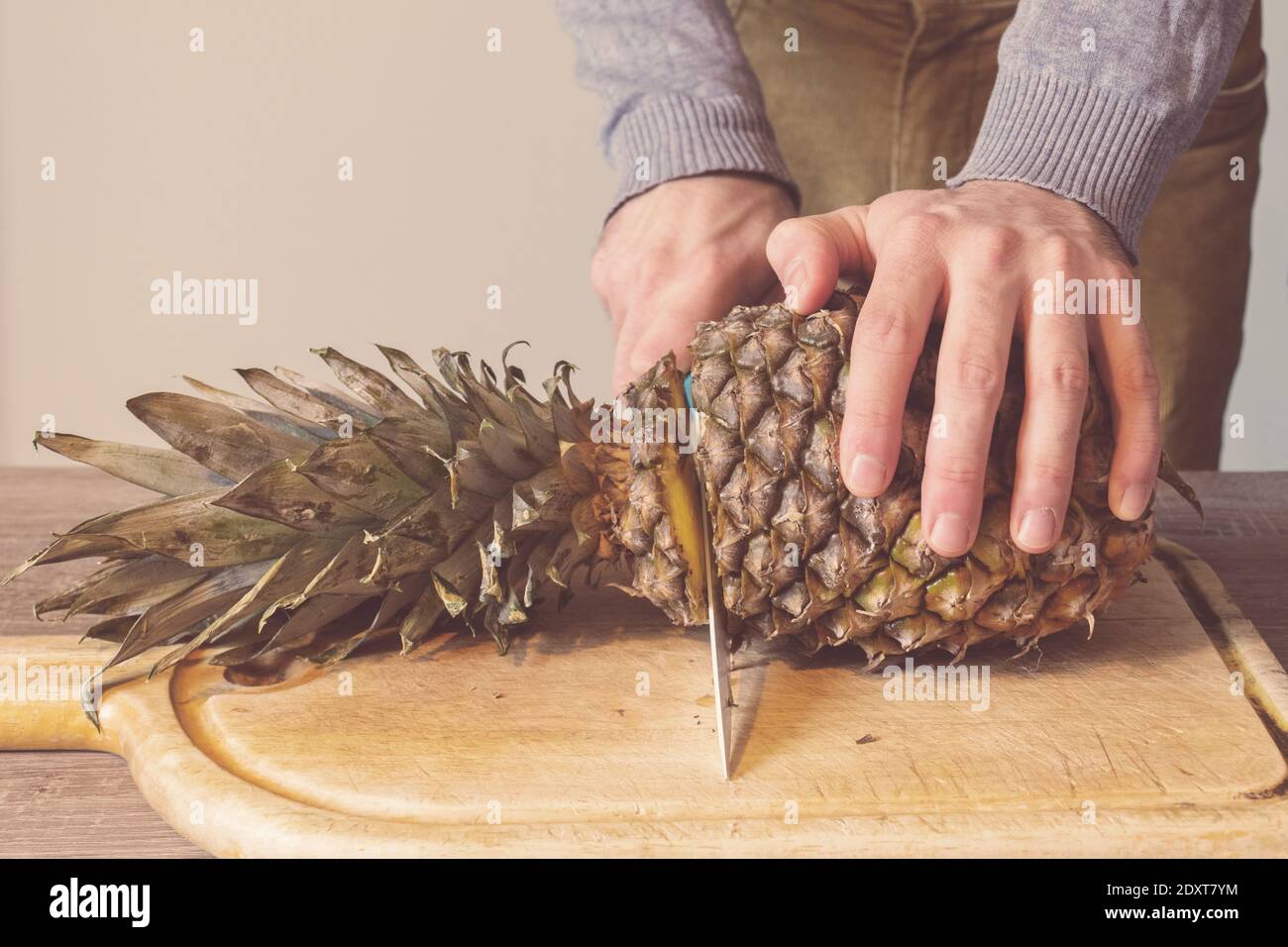 Man hands cutting a pineapple on a wooden table Stock Photo