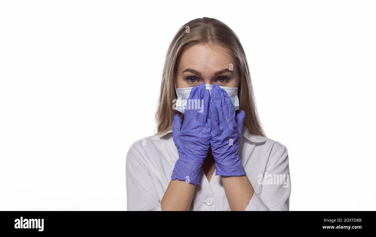 Correcting medical face mask young nurse with long straight hair looking at the camera wearing white medical uniform isolated on white background Stock Photo