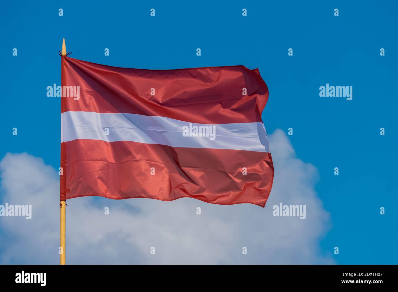 Flag of Latvia on blue and cloudy sky background flying in strong wind. Latvian national flag. Stock Photo