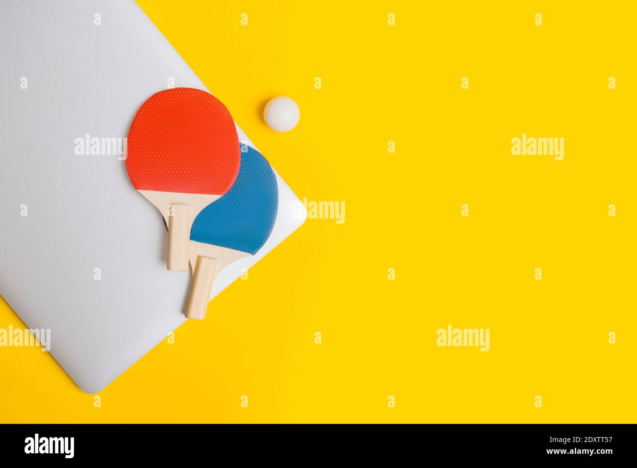 Table tennis racket, ball and grey laptop on yellow background. Online workout concept. Top view, space for your text Stock Photo