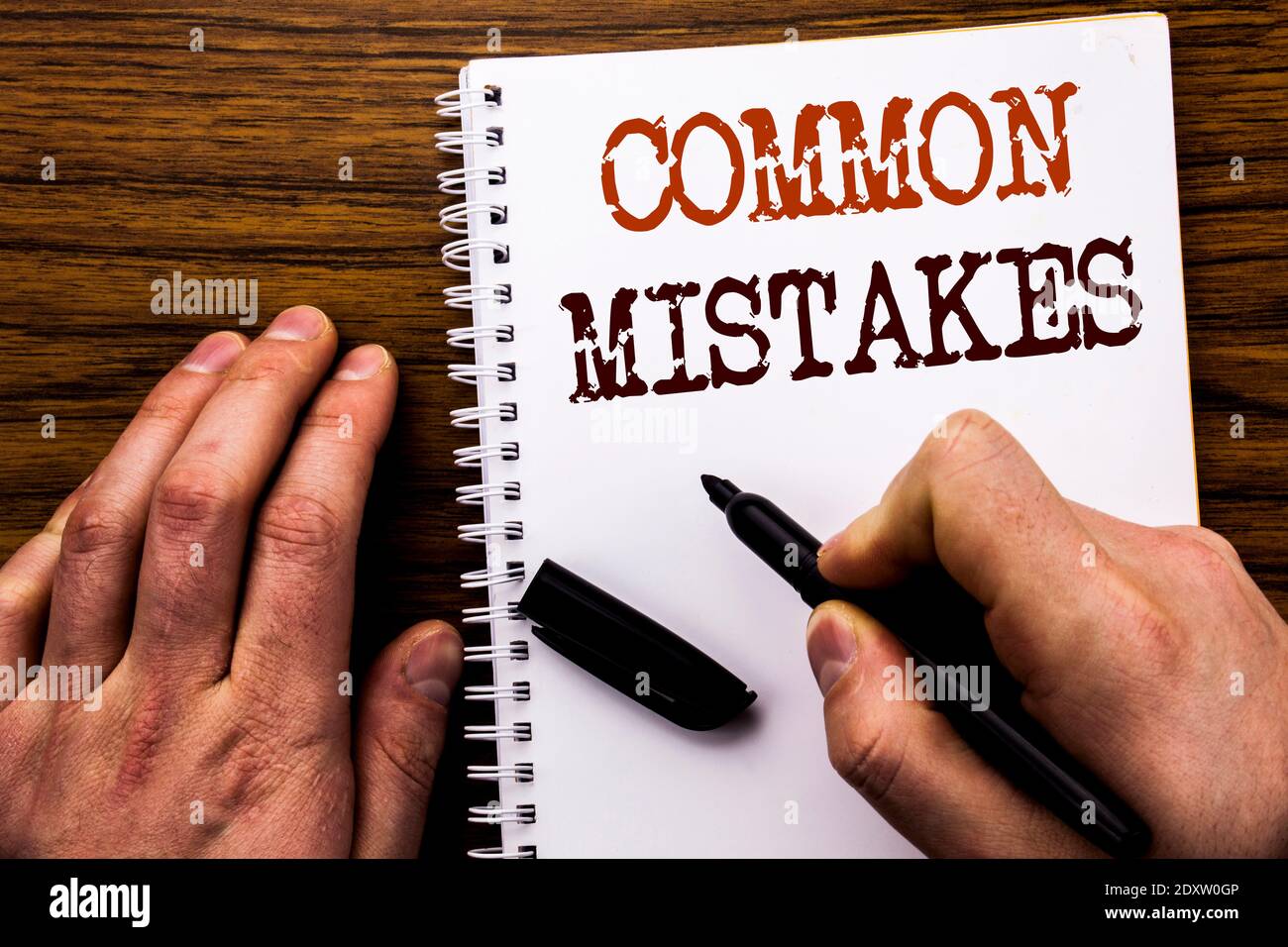 Cropped Hands With Common Mistakes Text On Spiral Notebook At Table Stock Photo