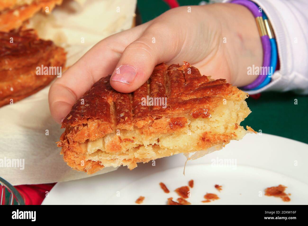 Portion of king cake in a child's hand above a plate and crumbs - Stock Image