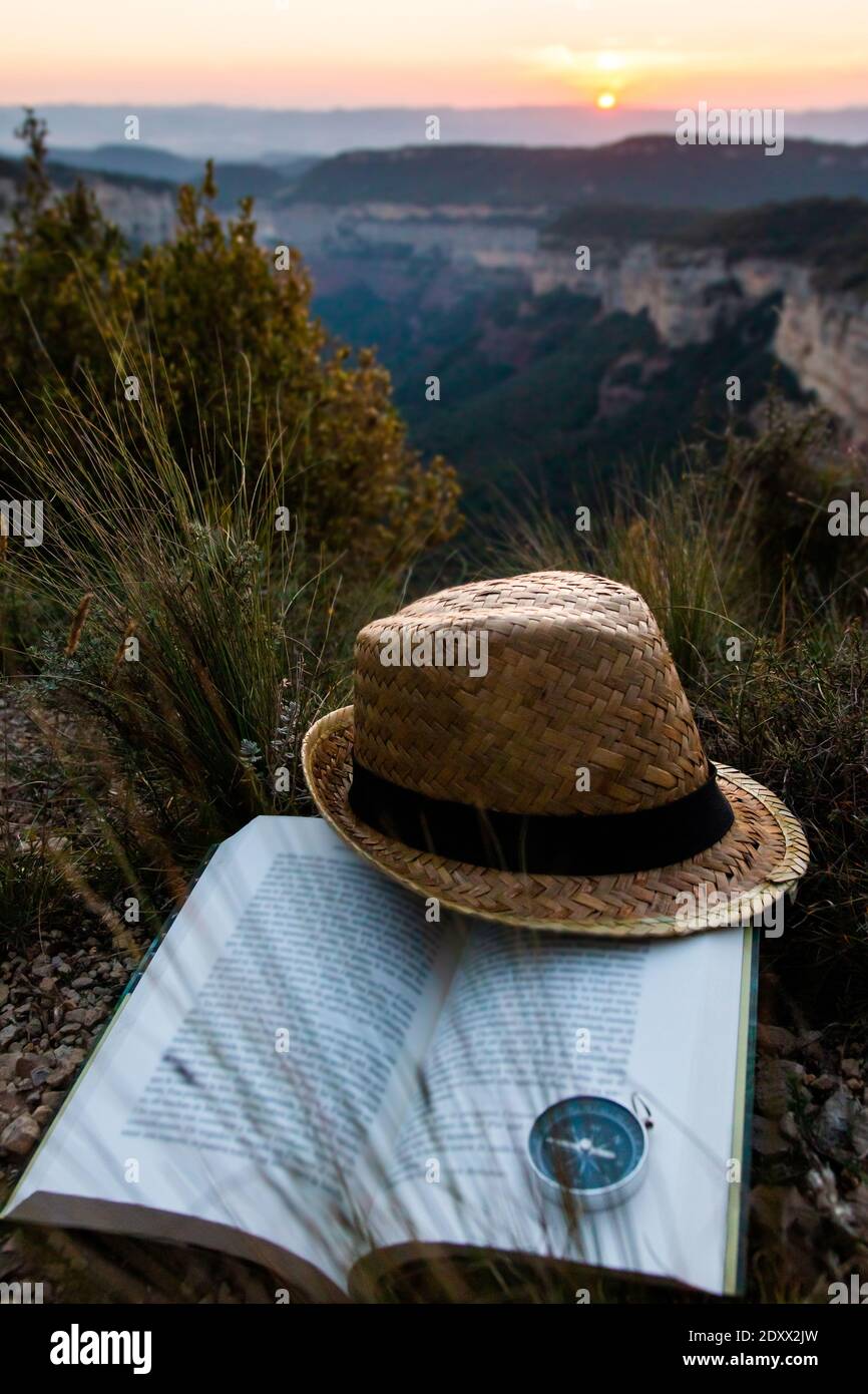 Travel concept. Straw hat with a travel adventure book on the mountain with sunset or sunrise in the background. Stories, imagination, disconnect from Stock Photo
