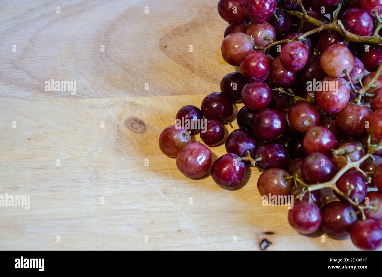 Looking down from above at a bunch of red grapes on a wooden chopping board. A shot with copy space which could be used as a background. Stock Photo